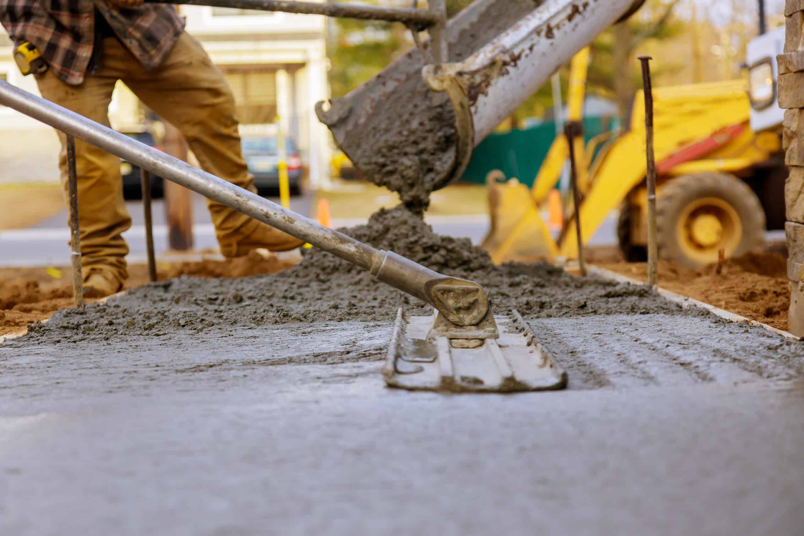 Worker pouring concrete pavement for ground at construction site.