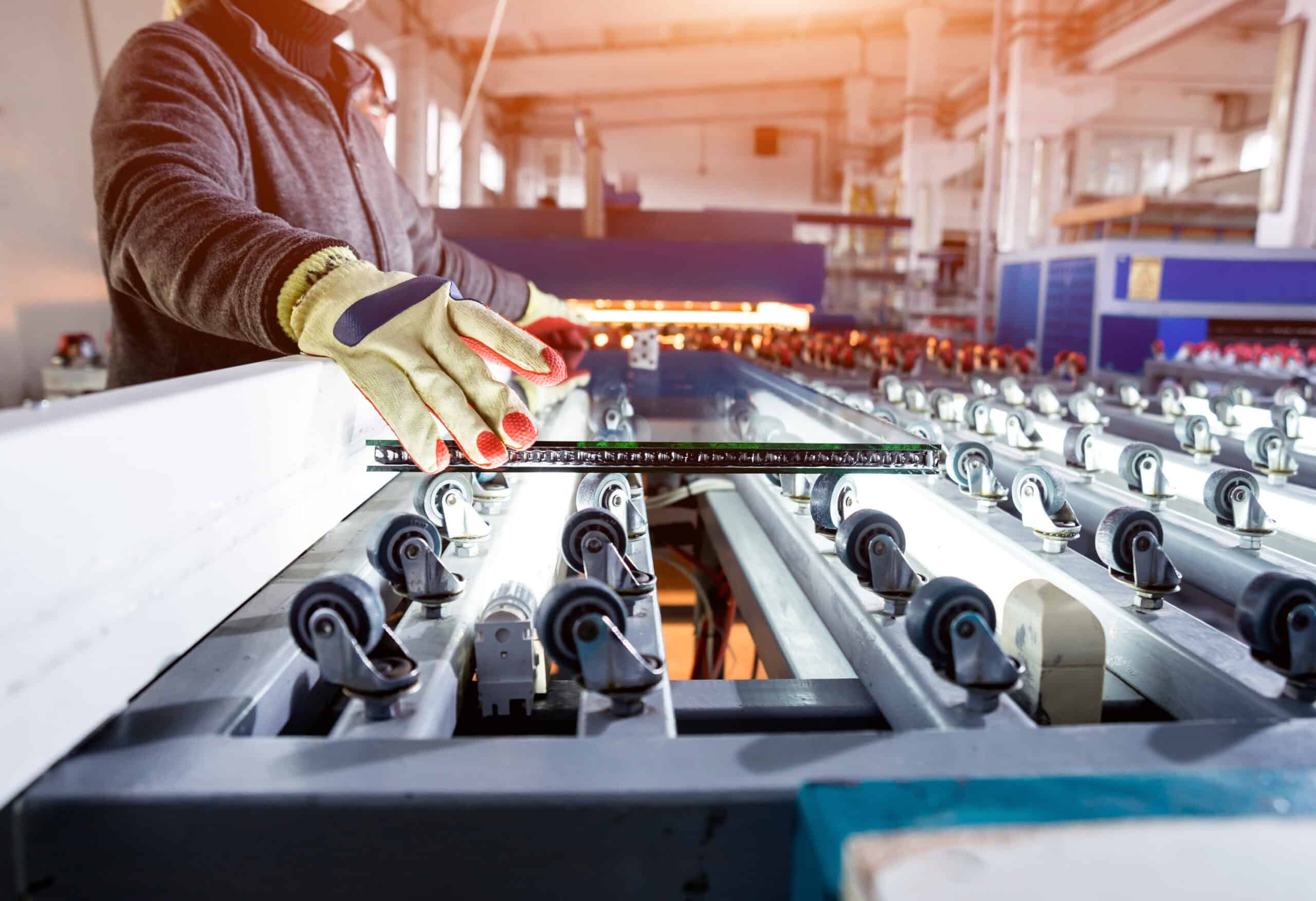 Industrial plant with worker and conveyer belt for production of a window pane.