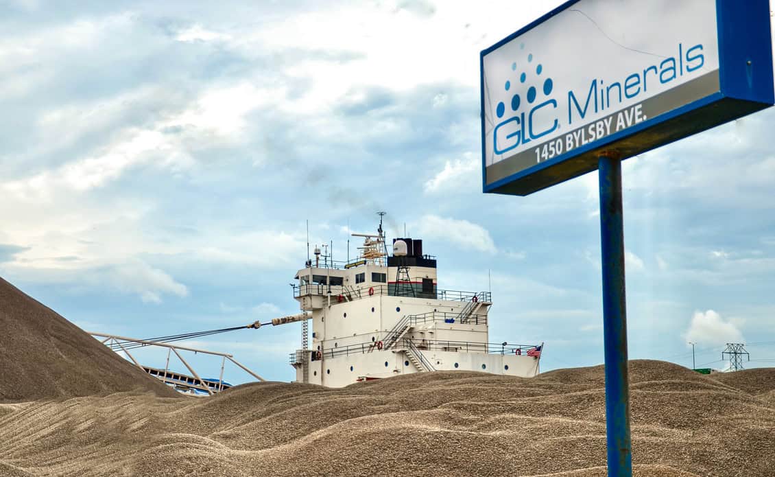 GLC Minerals sign with cargo ship and mineral piles behind it.